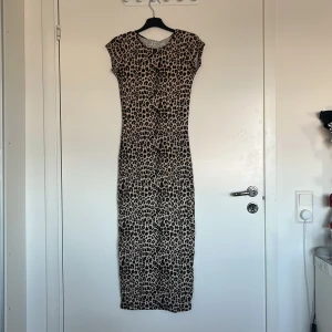 Leopardmönstrad klänning från lager 157 - Snygg leopardmönstrad klänning från lager i en tight passform. Klänningen är ärmlös och har en lång längd, perfekt för att sticka ut. Den är gjord i ett mjukt och bekvämt material som känns skönt mot huden.