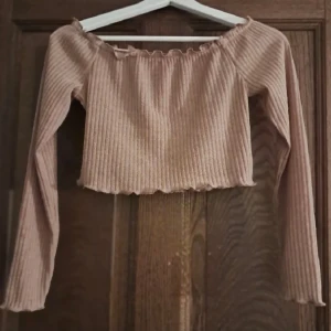 Beige ribbad offshoulder topp - Beige ribbad offshoulder topp med långa ärmar. Toppen är croppad och har en elastisk kant upptill för en bättre och mer bekväm passform. 