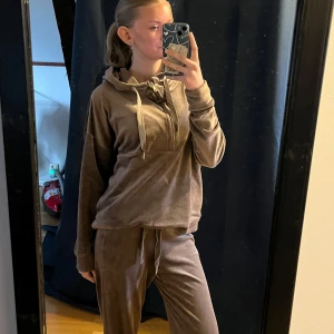 Lila myssett - Mysig lila hoodie i mysigt tyg med dragkedja och huva. Perfekt för en avslappnad stil. Den har långa ärmar och en praktisk ficka framtill. Även ett par matchande byxor till. 