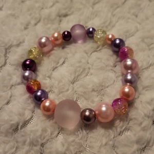 Färgglatt pärlarmband - Charmigt armband med pärlor i olika färger som rosa, lila och gult. Pärlorna har en glittrig och matt finish, vilket ger en lekfull och unik look. Perfekt för att lägga till en färgklick till din outfit.