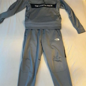 Grå tröja från The North Face - Säljer en grå tröja från The North Face med lång ärm och logga på bröstet. Perfekt för en avslappnad stil eller träning. Tröjan har en modern design och är tillverkad i ett bekvämt material.
