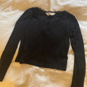Svart långärmad topp från H&M - Säljer en jätte gullig svart långärmad topp från H&M med spetsdetaljer vid halsringningen och en liten rosett framtill. Den har små design hål men inget som syns. Kontakta vid intresse/köp eller om ni har någon fråga🤗
