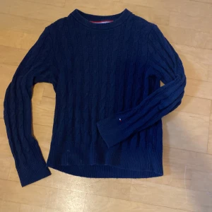 Mörkblå stickad tröja - Säljer en stilren mörkblå stickad tröja med kabelstickat mönster. Tröjan har långa ärmar och en rund halsringning. Passar till allt!                 Personen på bilden är 182 cm och tröjan sitter lite litet. Nytt pris ca 1200 kr, mitt pris 250 kr!