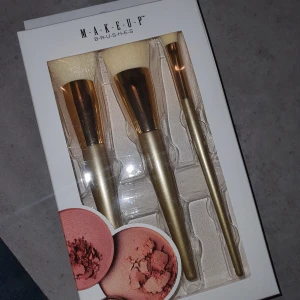 Makeupborstar i set - Set med tre makeupborstar i elegant design. Borstarna har gyllene handtag och vita borst, perfekta för applicering av olika sminkprodukter. 