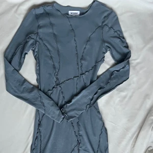 Grå klänning från Weekday - Snygg grå klänning från Weekday med unika sömdetaljer som skapar ett coolt mönster. Klänningen har en tight passform och långa ärmar, perfekt för en stilren look.