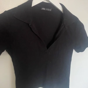 Svart polotopp från Zara - Säljer en stilren svart polotopp från Zara. Toppen har korta ärmar och en klassisk krage med v-ringning. Perfekt för en elegant och enkel look.