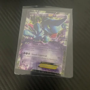 Toxicroak EX Pokémonkort - Säljer ett Toxicroak EX Pokémonkort med 170 HP. Kortet har attacker som Triple Poison och Smash Uppercut. Perfekt för samlare eller spelare som vill förstärka sin kortlek. Kortet är i en skyddande plastficka.