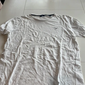 Vit t-shirt från GANT - Säljer en klassisk vit t-shirt från GANT med broderad logga på bröstet. T-shirten är kortärmad och tillverkad i mjuk bomull. Perfekt för en stilren och avslappnad look.