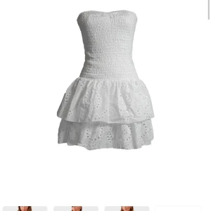 Vit axelbandslös klänning från Meet Me There - Söt vit axelbandslös klänning med smockad överdel och volangkjol. Den har inbyggda shorts och är perfekt till sommaren! 