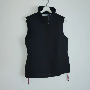 Svart väst från Race Marine - Snygg svart väst från Race Marine i storlek S. Västen har en dragkedja framtill och är tillverkad i 100% polyamid med polyesterfyllning. Perfekt för en stilren look.