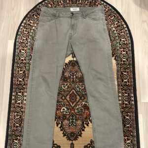 Grå jeansbyxor från Boss - Snygga grå jeansbyxor från Boss med en klassisk design. De har en normal passform och är perfekta för en stilren look. Byxorna har knappar och dragkedja framtill.