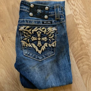 Bootcut miss me jeans - Snygga blå jeans från Miss Me med unika broderade detaljer på bakfickorna. Jeansen har en bootcut-stil och är dekorerade med knappar och en logotyp på baksidan. Lågmidjade. 