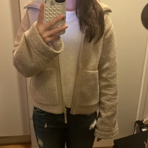 Beige teddyjacka med dragkedja - Mysig beige teddyjacka med dragkedja framtill. Jackan har långa ärmar och en bekväm passform, perfekt för kyligare dagar. Den fluffiga texturen ger en trendig look. Jackan är i storlek S och kommer ifrån HM❤️