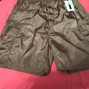 Bruna nylonshorts från H - Snygga bruna shorts i nylon från H. De har en elastisk midja och praktiska sidofickor. Perfekta för en avslappnad stil.