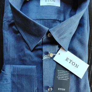 Blå skjorta från Eton - Snygg blå skjorta från Eton med klassisk krage och knappar framtill. Perfekt för en stilren look. Skjortan är tillverkad i ett högkvalitativt material som ger en lyxig känsla. Helt ny, inköpt för 1699kr. Mått: Total length: 84 cm Width from armpit to armpit: 69 cm Waist width: 68 cm Collar width: 51 cm Sleeve length from armpit: 53 cm