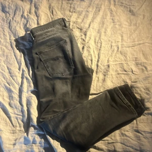 Svarta jeans från Nudie Jeans - Snygga svarta jeans från Nudie Jeans med klassisk femficksdesign och knappgylf. De har en stilren look med subtila sömmar på bakfickorna. Perfekta för en avslappnad stil.  Det är Grim Tim modellen. Storlek: W 30 L28. Priset kan duiskuteras😁