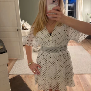 Vit prickig klänning - Charmig vit klänning med svarta prickar och v-ringad design. Liknar en slutsåld Zara klänning. Knappen vid v-ringningen kan användas för att ändra djupet på ringningen. Hör av er vid funderingar🤗🤗❤️❤️