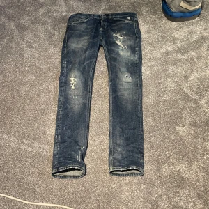 Blå jeans med slitningar - Säljer ett par blå jeans med coola slitningar och en vintage look. De har en klassisk femficksdesign och en bekväm passform. Perfekta för en avslappnad stil. Hör gärna av dig vid frågor eller så!