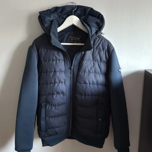 Mörkblå cardigan jacka från Ombre - Snygg mörkblå cardigan jacka från Ombre med huva och dragkedja. Jackan har långa ärmar och ribbade muddar vid ärmslut och nederkant. Perfekt för kyligare dagar.