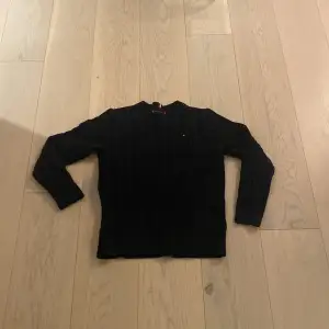 Säljer en stilren svart stickad tröja från Tommy Hilfiger. Tröjan har ett klassiskt flätmönster och en liten logotyp på bröstet. 
