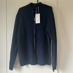 Mörkblå kofta från LMTD - Säljer en stilren mörkblå kofta från LMTD. Den har en dragkedja framtill och är ribbad i materialet. Perfekt för kyligare dagar och passar bra till både jeans och kjol. Ett måste i garderoben för den som gillar klassiska plagg.