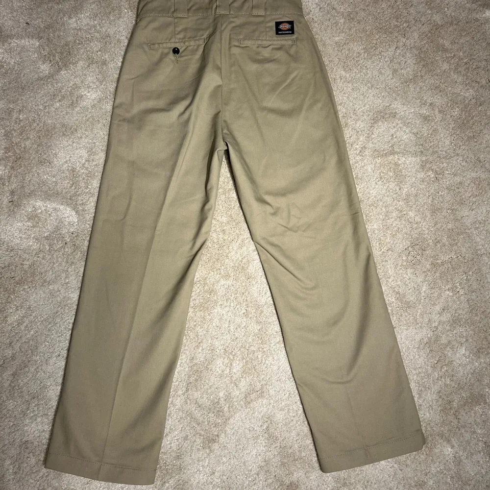 Snygga beige byxor från Dickies med en klassisk design. Byxorna har en rak passform och är tillverkade i ett slitstarkt material. Perfekta för en avslappnad stil. De har en knapp och dragkedja framtill samt en bakficka med knapp.. Farkut & Housut.