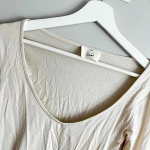Beige långärmad topp från A_DSGN - Säljer en stilren beige långärmad topp från A_DSGN. Den är i ett mjukt och bekvämt material. Exakt samma topp som jag säljer i brunt fast i beige. Toppen har en enkel design med rund halsringning och är i storlek M.