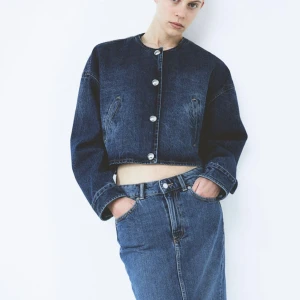 Mörkblå croppad jeansjacka - Säljer en supercool mörkblå croppad jeansjacka med stora silverknappar. Jackan har en avslappnad passform och två snedställda fickor fram. Perfekt för en casual look! Aldrig använd