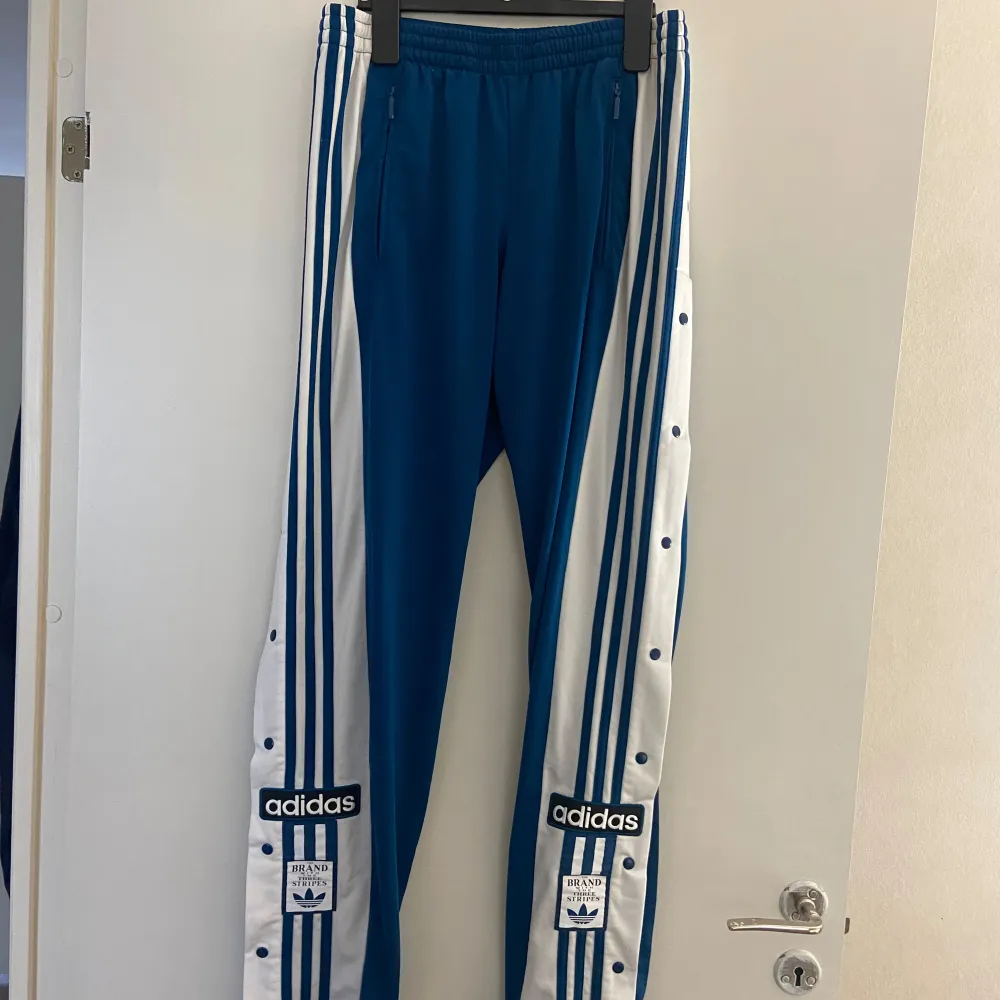 Adidas Adibreak byxor i storlek M Knappar längs benen som går att knäppa upp. Använd ett fåtal gånger, säljs pga att de inte inte kommer till användning längre.  Så coola!. Jeans & Byxor.