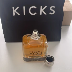 In Love With You Parfym - Säljer en lyxig parfymflaska från Emporio Armani, 'In Love With You'. Flaskan är elegant och genomskinlig med en varm bärnstensfärgad vätska inuti. Den har en stilren silverfärgad kork som ger en exklusiv känsla. Perfekt för den som vill ha en doft som utstrålar kärlek och elegans. Kommer från KICKS.