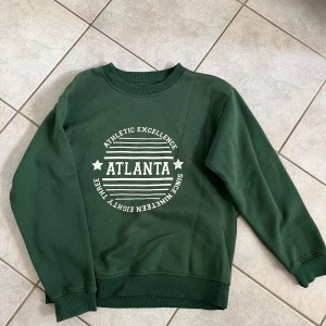 Grön sweatshirt från Daisy Street - Säljer en snygg grön sweatshirt från Daisy Street med trycket 'Atlanta Athletic Excellence' i vitt på framsidan. Tröjan är i storlek XS och har en normal passform med långa ärmar. Perfekt för en avslappnad stil eller för att mysa hemma. skriv vid frågor💗