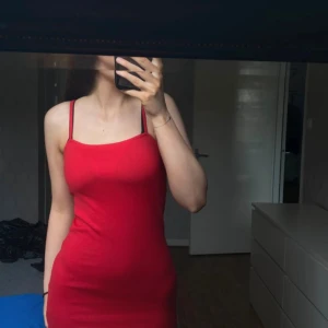 Röd tight klänning - Säljer en snygg röd klänning med smala axelband. Den är tight och perfekt för festliga tillfällen. Klänningen är ärmlös och har en enkel men stilren design.