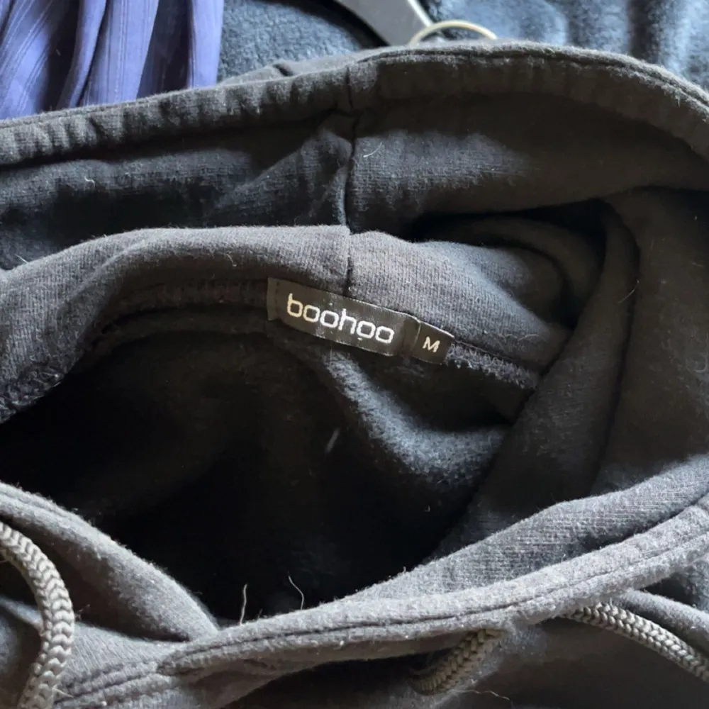 Säljer en svart hoodie från Boohoo i storlek M. Den har ett coolt blått hjärtmönster med texten 'Design Studio' på baksidan. Perfekt för en avslappnad stil och passar bra till både jeans och joggers. Hoodien har långa ärmar och en klassisk huva med dragsko.. Tröjor & Koftor.