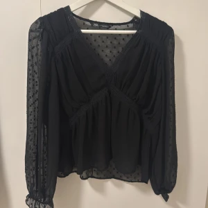 Svart blus från Zara - Elegant svart blus från Zara med långärmad design. Blusen har ett diskret prickigt mönster och spetsdetaljer.