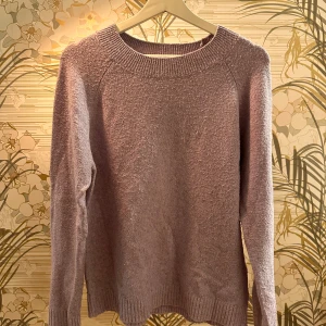 Lila stickad tröja - Mysig lila stickad tröja med rund halsringning och långa ärmar. Perfekt för kyligare dagar och ger en avslappnad stil. Ribbstickade muddar vid ärmslut och nederkant för extra komfort.