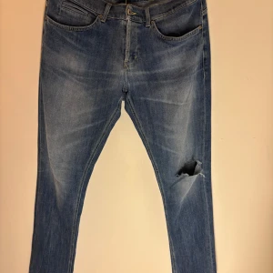 Dondup George jeans med slitningar - Snygga blå jeans med en cool slitning på ena benet. De har en klassisk femficksdesign och en knappgylf. Perfekta för en avslappnad stil. Inga defekter toppskick, passar 180-190 cm lång vikt spelar ingen roll