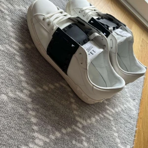 Valentino skor - Snygga vita sneakers från Valentino med svarta detaljer och nitar. Skorna har en klassisk design med snörning och en unik stil tack vare de svarta panelerna och nitarna på sidorna.