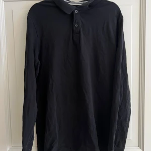 Svart pikétröja från Pier One - Snygg svart pikétröja från Pier One med krage och knappar framtill. Perfekt för en stilren look. Långärmad design som passar bra till både vardag och mer uppklädda tillfällen.