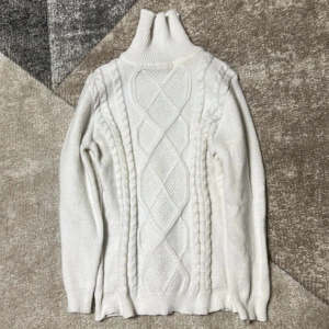 Vit stickad polotröja - Säljer en stilren vit stickad polotröja med ett snyggt flätmönster på framsidan. Tröjan har långa ärmar och en hög polokrage som håller dig varm under kyliga dagar. Perfekt för både höst och vinter!