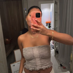 Beige tubtopp - Säljer en stilren beige tubtopp med ribbad textur och volangdetaljer vid nederkanten. Perfekt för varma dagar och kan enkelt matchas med olika outfits.