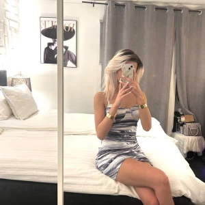 Mönstrad klänning i blå och vit - Snygg klänning med ett unikt mönster i blått och vitt. Den har en tight passform och är ärmlös, perfekt för en kväll ute. Klänningen har en stilren design med en v-ringad detalj framtill.