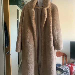 Beige teddyjacka strl 36 - Säljer en mysig beige teddyjacka med lång längd och långa ärmar. Perfekt för att hålla sig varm under kyliga dagar. Jackan har en klassisk design.