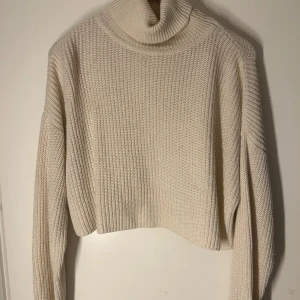 Beige stickad polotröja från BikBok - Säljer en mysig beige stickad polotröja från BikBok. Tröjan har en croppad passform och långa ärmar, perfekt för kyliga dagar. Den ribbade strukturen ger en stilren look. Passar utmärkt till både jeans och kjol.
