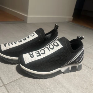 Dolce & Gabbana skor - Snygga svarta sneakers från Dolce & Gabbana med vit text på ovansidan. Skorna har en elastisk passform och en robust sula för extra komfort. Har vanligtvis 37/38 på skor och dessa passar perfekt! 🙌🏼