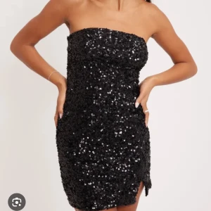 Svart paljettklänning - Snygg svart axelbandslös klänning täckt med glittriga paljetter. Perfekt för en kväll ute med vänner eller en speciell fest. Den korta längden ger en trendig look och den tighta passformen framhäver figuren. Ett måste för garderoben om du älskar att glänsa!