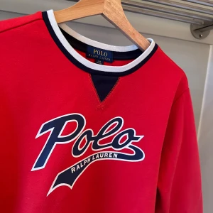 Röd sweatshirt från Polo Ralph Lauren  - Säljer en snygg röd sweatshirt från Ralph Lauren med stort Polo-tryck på framsidan. Tröjan har långa ärmar och en kontrasterande krage i svart och vitt. Perfekt för en avslappnad stil. Ny pris: 1195kr