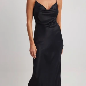 Svart långklänning i satin - Elegant svart långklänning i satin med smala axelband och en stilren design. Klänningen har en draperad halsringning. Perfekt för speciella tillfällen. Den är aldrig använd med saknar prislapp🥰😚