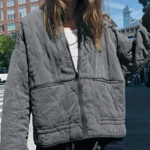 Grå quiltad jacka med dragkedja - Snygg grå quiltad jacka med krage som knäpps med dragkedja från Zara i storlek S. Kan nog även passa både mindre och större storlekar. Finns en dragsko nertill. Har använts en del men är fortfarande i fungerande skick. Skicket är som på bilderna, finns några tecken på användning, men helheten är fin. Trendig och passar till allt möjligt. Tyget är mjukt och skönt. 