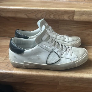 Vita sneakers med svarta detaljer - Snygga vita sneakers från Philippe Model med svarta detaljer på hälen. Skorna har en klassisk design med snörning och en robust sula. Perfekta för en stilren look. 8.5/10 skick box ingår! Tar gärna emot byten!!