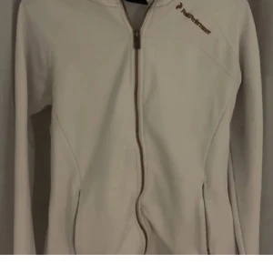 Vit hoodie zip up från Peak Performance - Säljer en stilren vit zip up hoodie från Peak Performance med dragkedja och huva. Hoodien har långa ärmar och är perfekt för en sportig look. Den är tillverkad i ett mjukt material som ger en bekväm passform.